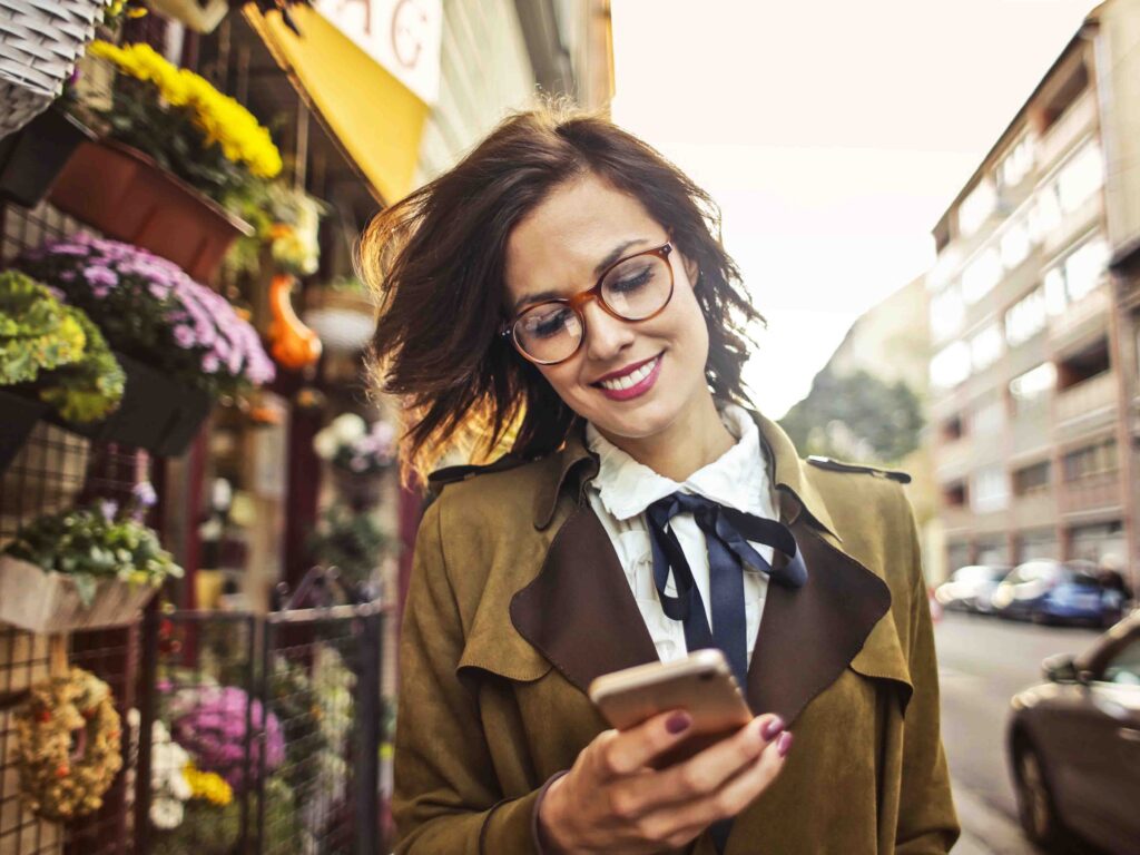Siti internet. Sito vetrina, donna che passeggia in una via con negozi e sorride mentre guarda il cellulare.