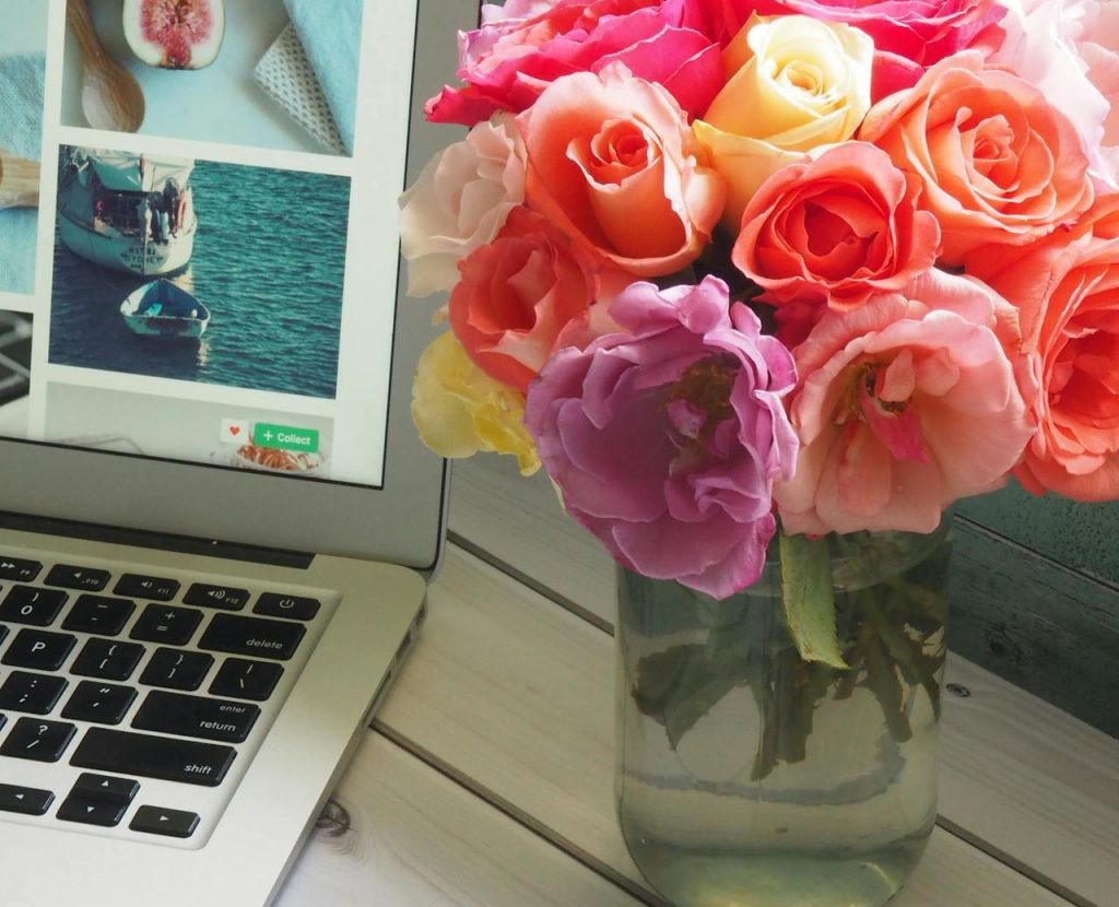 Pc portatile con foto, vaso di fiori colorati e riviste su tavolo. Cos’è un Blog Aziendale