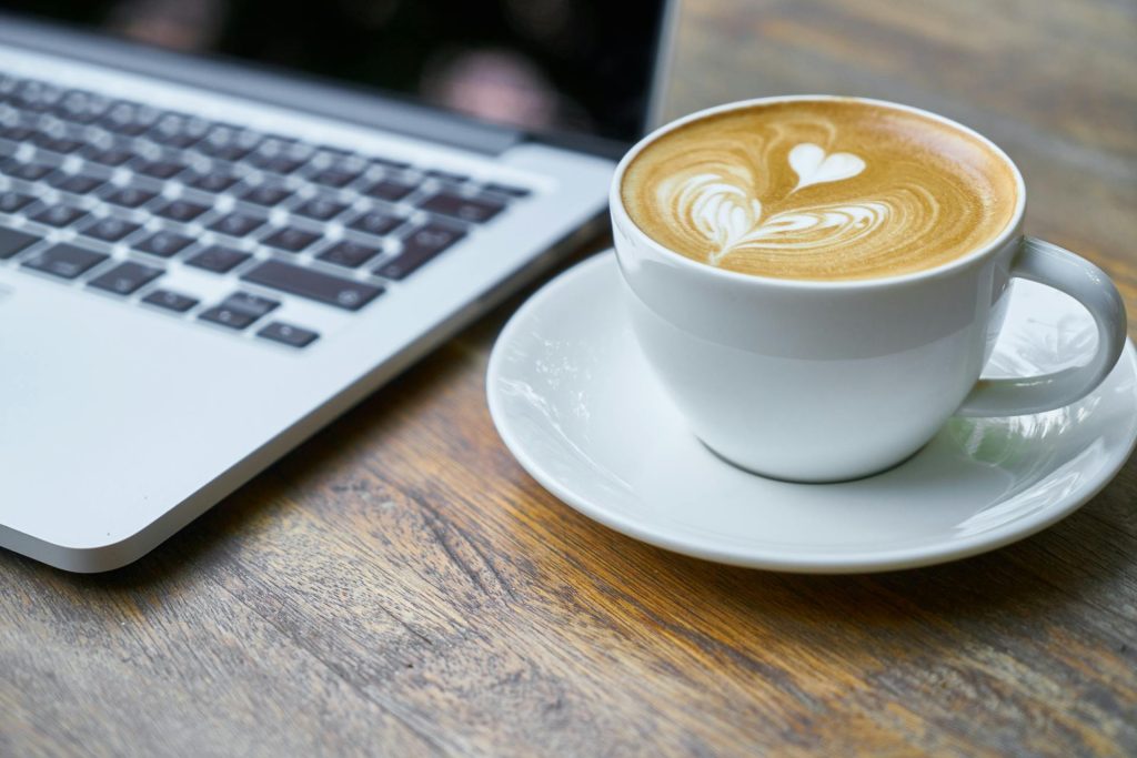 Tazza di cappuccino con schiuma a cuore, sullo sfondo pc portatile. Cos’è un Blog Aziendale