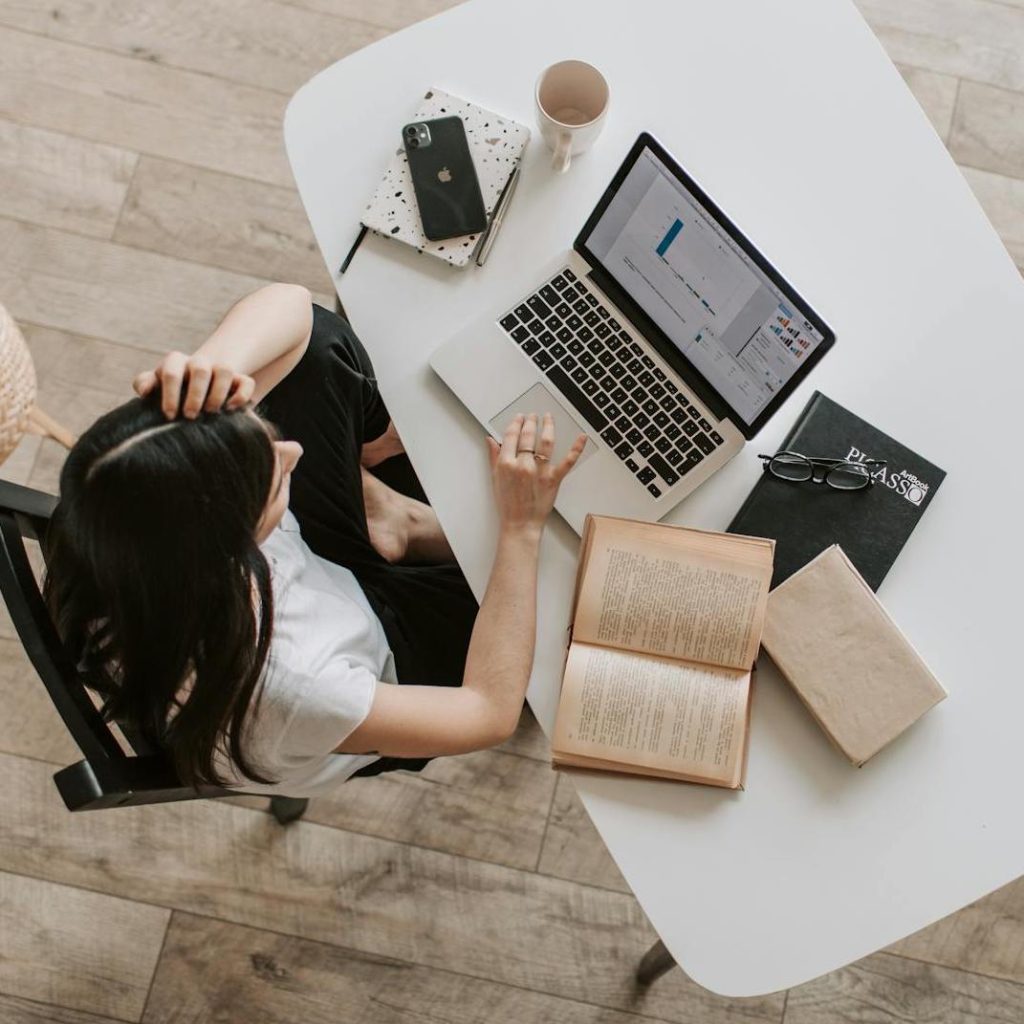 ragazzza con scrivania, pc portatile, libri, telefono e agenda, vista dall'alto. Cos’è un Blog Aziendale